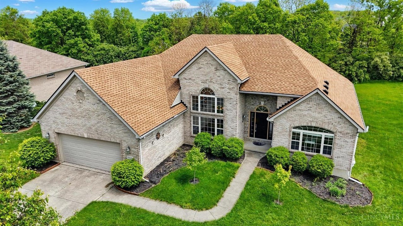 Two-story brick home with manicured lawn and attached garage in Liberty Township, Ohio, surrounded by green trees.